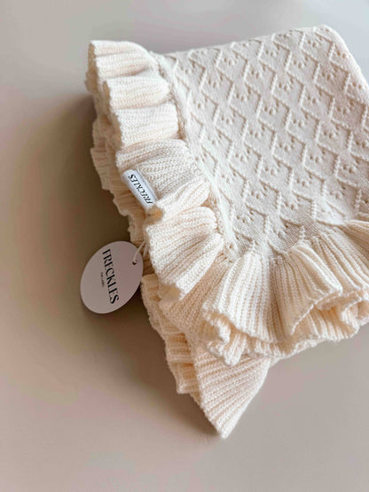 Knitted baby blanket with ruffled edge on a light background